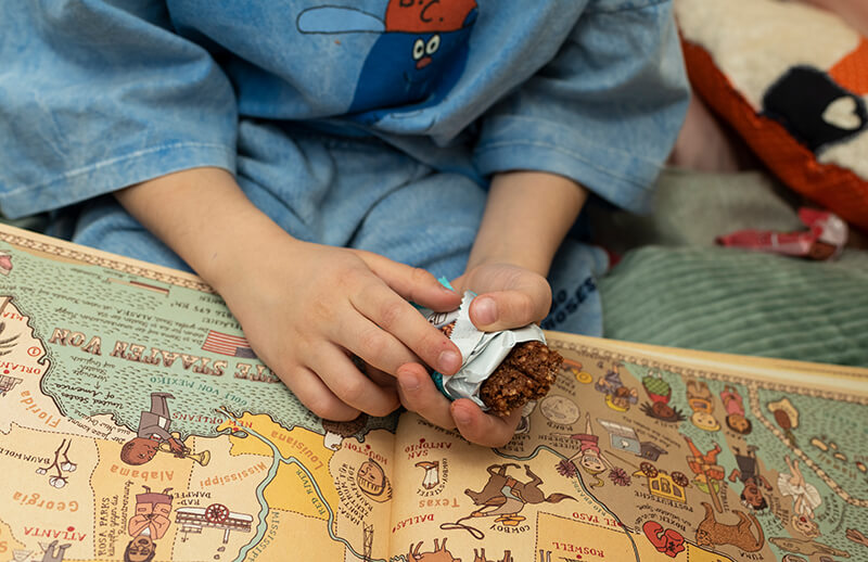 Kinder schauen sich Bücher an und essen das FruchtBar Knusper Duo